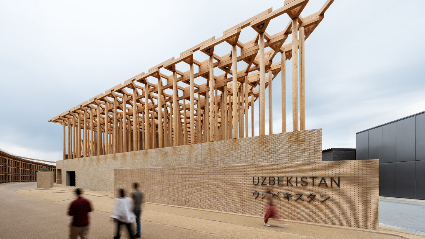 Exterior of the Uzbekistan Pavilion showing timber colonnade above a brick base with visitors walking past.