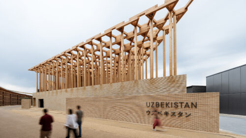 Exterior of the Uzbekistan Pavilion showing timber colonnade above a brick base with visitors walking past.