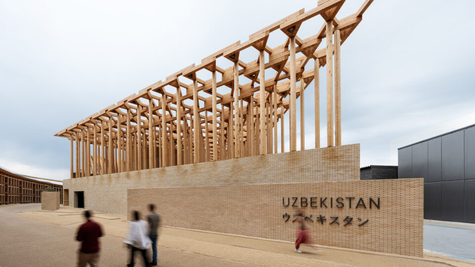 Exterior of the Uzbekistan Pavilion showing timber colonnade above a brick base with visitors walking past.