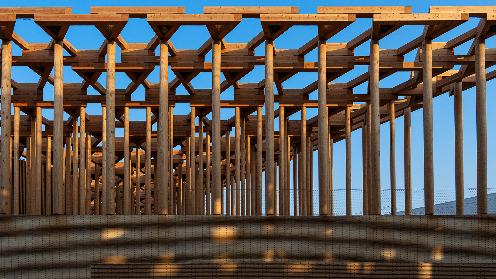 Detail view of interlocking timber columns and beams in the Uzbekistan Pavilion against a blue sky.
