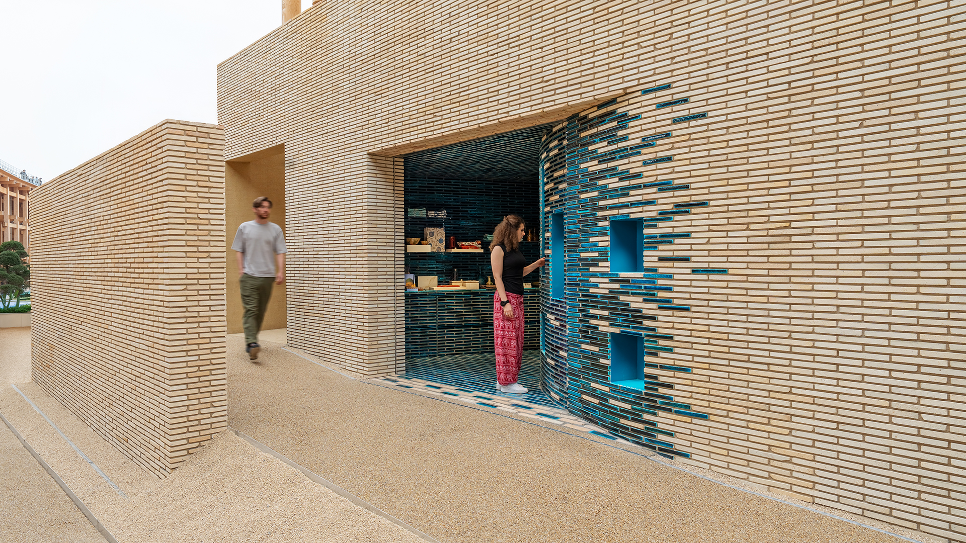 Entrance to the pavilion with detailed brick and tile patterns; a woman interacts with a display niche.