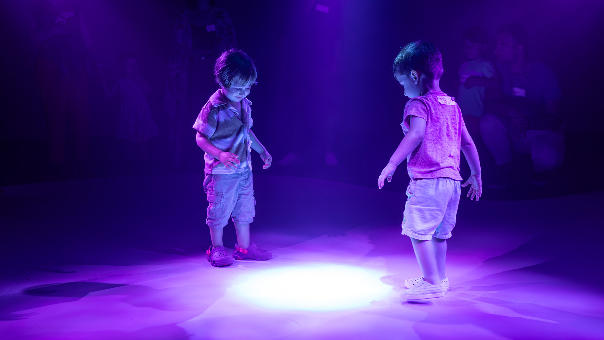 Two children interact with a glowing floor projection in the Colors of Creation immersive experience at The Weitzman.